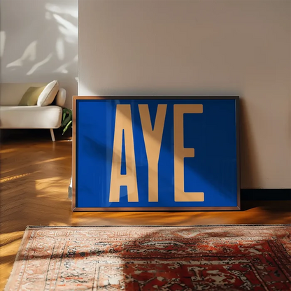 Aye Typography Quote Print - Peach framed, leaning on a wooden floor beside a rug