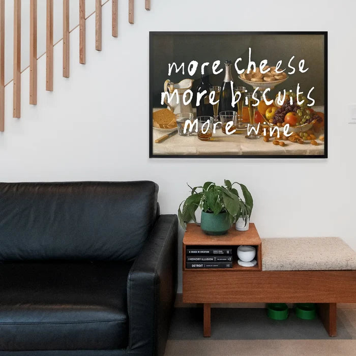 More Cheese Biscuits Wine Quote Print framed above a living room sofa