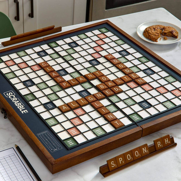 Scrabble board game on a table with tiles and a plate of cookies in the background